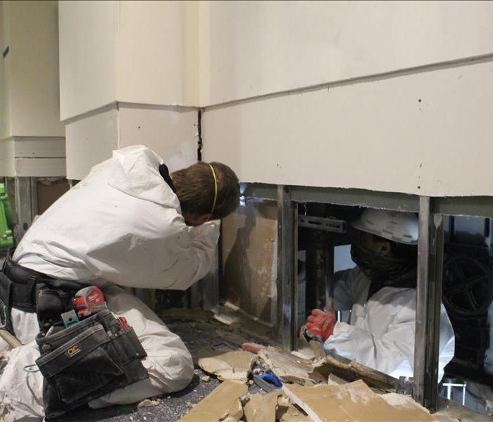 two males in white ppe suits with masks perform flood cut to water damage drywall, remove wall, restoration water damage 